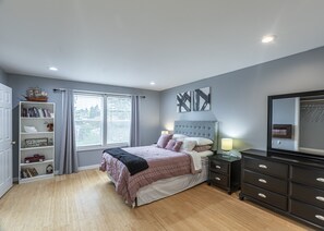 Une chambre à coucher comprenant un lit, une table de chevet, une commode, une bibliothèque et une fenêtre avec des stores.