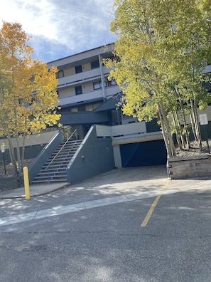 A parking garage entrance with a staircase leading to an upper level, surrounded by trees with yellow leaves.