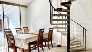 A dining area with a table set for six, wooden chairs, a black spiral staircase, and a white textured ceiling. - 3 min Walk to Slopes, Great Views, Shared Hot Tub  (Frisco)