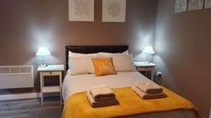 A neatly made bed with striped bedding and a single decorative pillow, flanked by two bedside tables with lamps, in a room with a radiator and a wall-mounted outlet. - Modern 1-Bed Apartment – 3 Min Walk to HOST & Pitman, Leeds (Leeds)