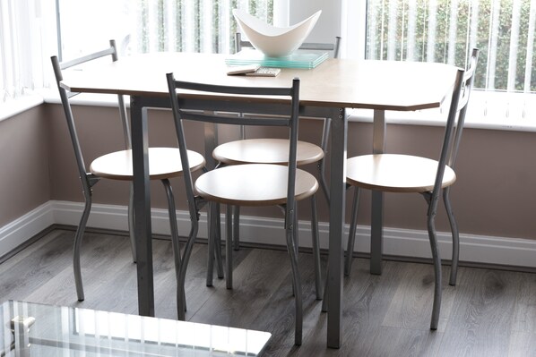 A dining area with a table and four chairs, a bowl on the table, and a window with blinds. - Modern 1-Bed Apartment – 3 Min Walk to HOST & Pitman, Leeds Arena (Leeds)