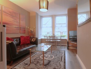 A modern living room with a leather sofa, glass coffee table, and a dining area with a white table and chairs. - Modern 1-Bed Apartment – 3 Min Walk to HOST & Pitman, Leeds Arena (Leeds)