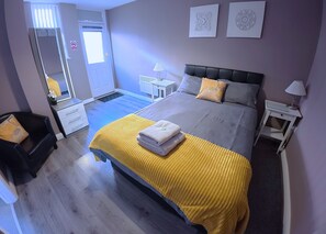 A hotel room with a bed, a chair, a desk, a mirror, and a door. - Modern 1-Bed Apartment – 3 Min Walk to HOST & Pitman, Leeds Arena (Leeds)