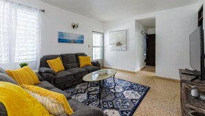 Ein Wohnzimmer mit grauem Sofa, gelben Kissen, einem Couchtisch und einem gemusterten Teppich.