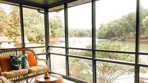 Una habitación con grandes ventanales que dan a un río, muebles de mimbre y una mesa redonda.