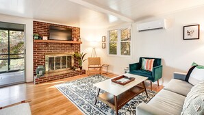 Una sala de estar con chimenea de ladrillo, un sofá verde, un sofá blanco y una mesa de centro.