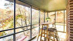 Una habitación con ventanas amplias, una mesa de madera y taburetes de bar.