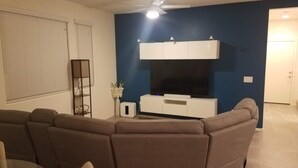 Ein Wohnzimmer mit einer Eckcouch, einem Flachbildfernseher auf einer weißen Unterhaltungseinheit und einem Deckenventilator.