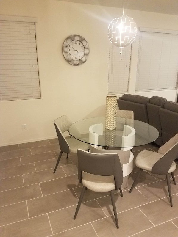 A dining area with a glass table surrounded by chairs, a clock, and a decorative light fixture.