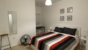 Une chambre à coucher avec un lit, un ventilateur sur pied, un bureau et une chaise.