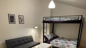 Une petite pièce meublée, avec un lit superposé, un canapé, une table et un fauteuil poire.