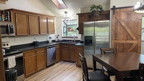 A kitchen with wooden cabinets, stainless steel appliances, a dishwasher, and a dining area with a table and chairs.
