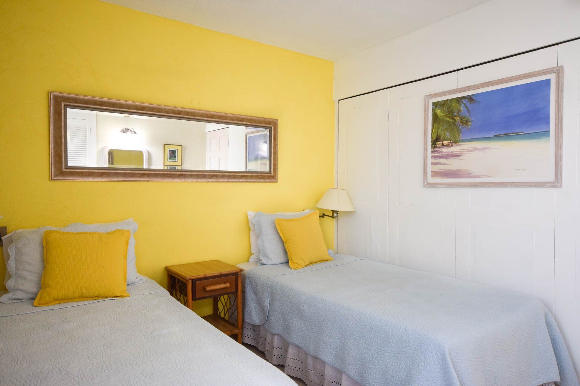 Una habitación con dos camas, un espejo, un cuadro de playa y una mesita de noche de madera.
