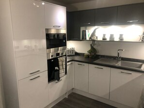 A modern kitchen with white cabinets, a built-in oven, and a stainless steel range hood.