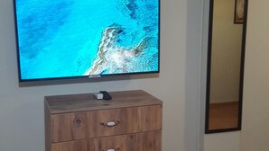 Ein Zimmer mit einem Holzkleiderschrank, einem Flachbildfernseher, einer Wanduhr und einem Spiegel.