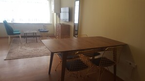 Ein Essbereich mit Holztisch und Drahtstuhlen, ein blau gepolsterter Sessel, ein kleiner runder Tisch und eine Heizung.