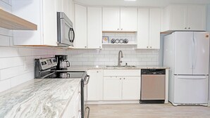A modern kitchen with white cabinets, a stainless steel microwave, a built-in oven, a dishwasher, and a white refrigerator. - Cheerful 2 Bedroom Townhome With Fireplace & Private Patio  in New Smyrna Beach! (New Smyrna Beach)