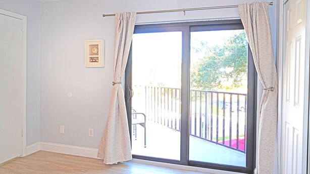 A room with a sliding glass door leading to a balcony with a metal railing. - Cheerful 2 Bedroom Townhome With Fireplace & Private Patio  in New Smyrna Beach! (New Smyrna Beach)