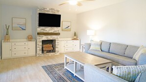 A living room with a fireplace, a sofa, a coffee table, and a TV mounted on the wall. - Cheerful 2 Bedroom Townhome With Fireplace & Private Patio  in New Smyrna Beach! (New Smyrna Beach)