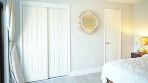 A bedroom with a bed, a white door, a round mirror, and a nightstand with a lamp. - Cheerful 2 Bedroom Townhome With Fireplace & Private Patio  in New Smyrna Beach! (New Smyrna Beach)