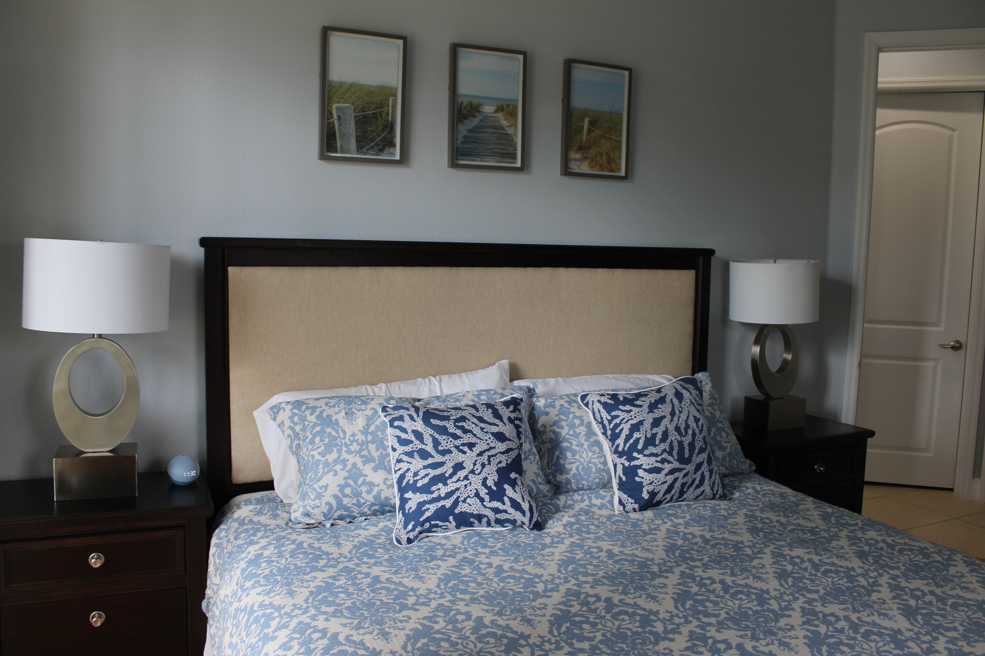A bedroom with a bed, two nightstands, a wooden headboard, and three framed pictures on the wall.