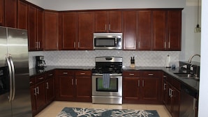 A kitchen with wooden cabinets, stainless steel appliances, a tiled backsplash, and a blue rug. - Family friendly house, w/ elevator, hot tub, and easy walk to beach! (Indian Shores)