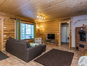 A log cabin interior with a sofa, TV, fireplace, and a view of the outside.