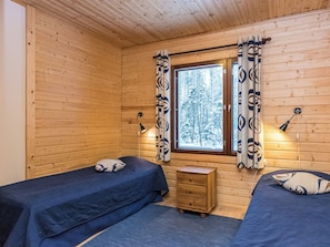 A cabin room with two beds, a small wooden nightstand, and a window with curtains.