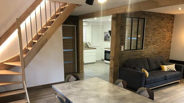 A modern living space with a dining area, a staircase, a kitchen, and a stone accent wall.