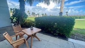 Un espace extérieur aménagé avec une table et des chaises, entouré de verdure et offrant une vue sur une pelouse bien entretenue et des bâtiments situés au loin.