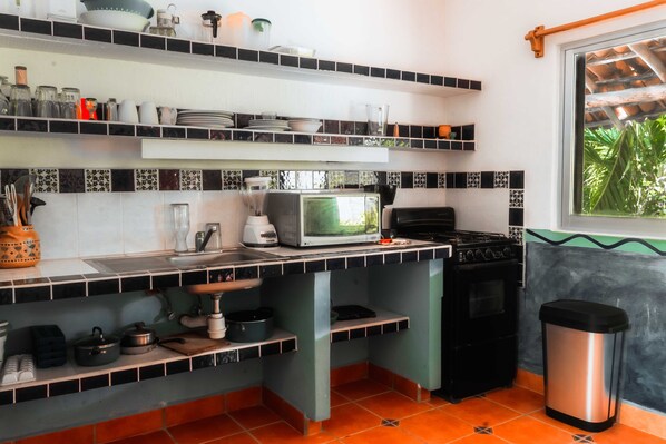 Une cuisine avec un dosseret carrelé en noir et blanc, un four à micro-ondes, une cuisinière et divers ustensiles de cuisine.