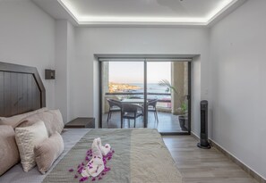 Quarto com cama, mesa de cabeceira, janela com vista para a praia e varanda com mesa e cadeiras.