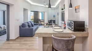 A modern apartment with a kitchen area featuring a built-in oven, a dining table with chairs, a sofa, and a balcony with a view. - AWESOME OCEAN VIEWS, GREAT LOCATION, PERFECT VACATION (Cabo San Lucas)