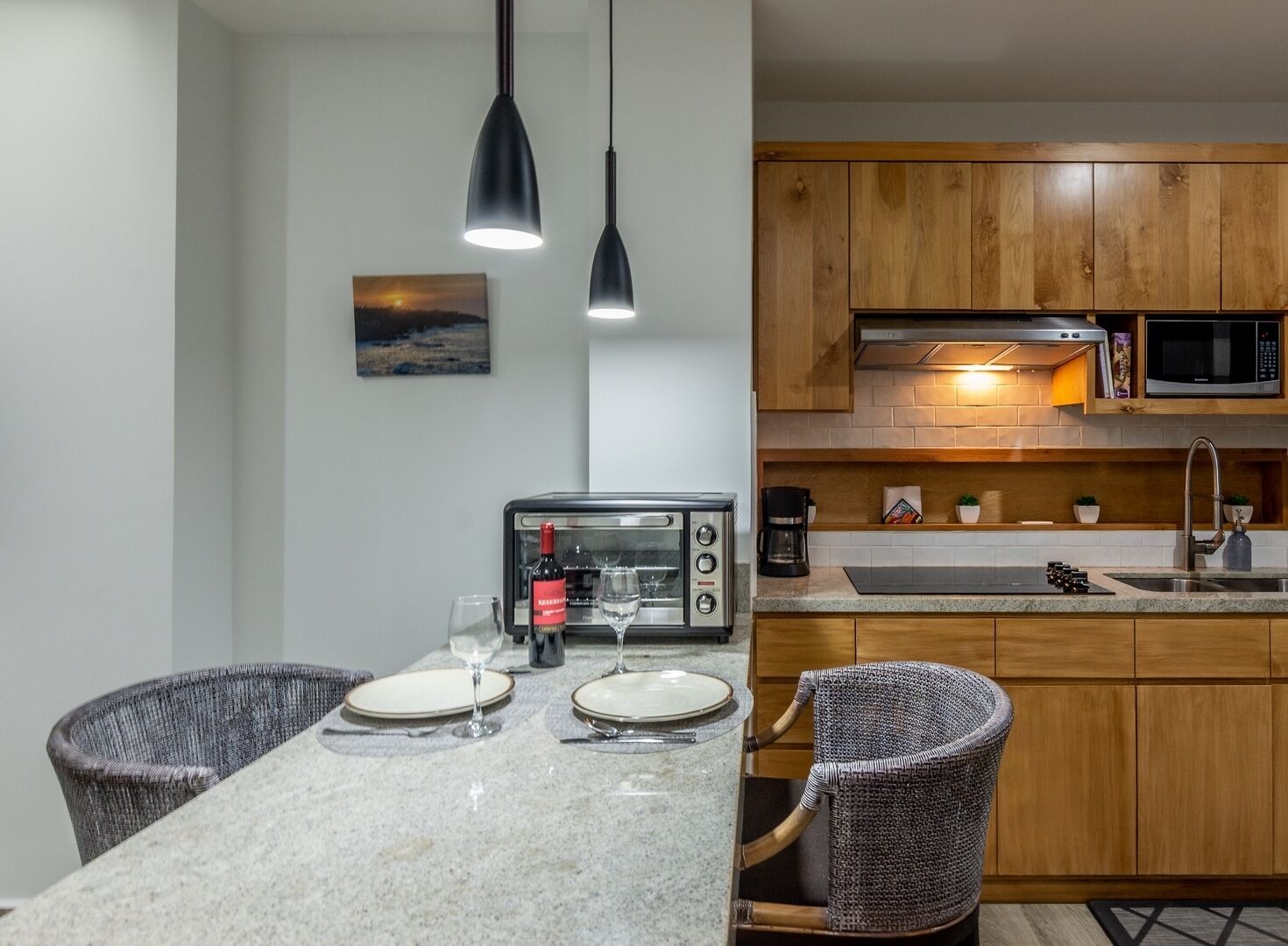 Eine moderne Küche mit Holzausstattung, einer eingebauten Mikrowelle, einem Toaster und einem Spülbecken. Ein Esstisch mit Stühlen und einem Weinglas sind ebenfalls vorhanden.