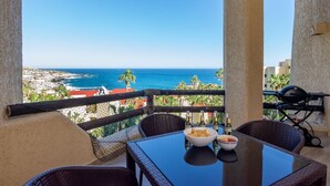 A balcony with wicker furniture, a table with bowls of food and drinks, and a view of the ocean and buildings. - AWESOME OCEAN VIEWS, GREAT LOCATION, PERFECT VACATION (Cabo San Lucas)