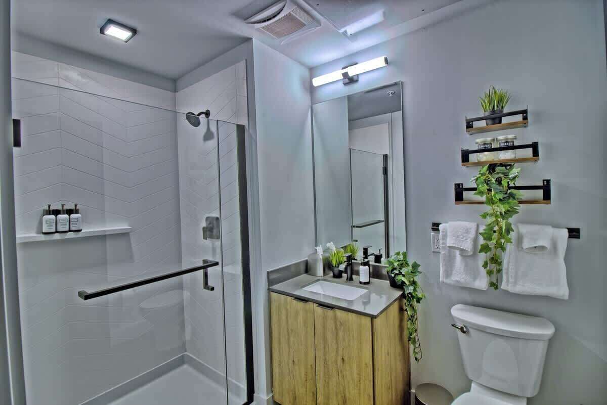 A modern bathroom with a shower, toilet, and sink, featuring a mirror, towel rack, and plant decorations.