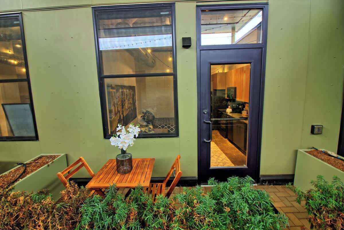Ein schlichtes, modernes Gebäude mit einem Essbereich, der einen Holztisch, Stühle, eine Vase mit weißen Blumen und einen Blick ins Innere durch eine Glastür bietet.