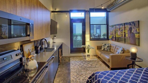 A modern kitchen with a built-in oven, a dining area with a sofa, and a large window with a view. - Chic Ultramodern Minimalist Studio Loft + Patio (Saint Louis)