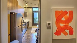 A narrow hallway with a kitchen area, a modern art piece, and a visible door leading to another room. - Chic Ultramodern Minimalist Studio Loft + Patio (Saint Louis)
