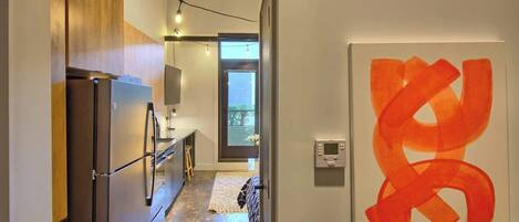 Un pasillo estrecho con una zona de cocina, una obra de arte moderno y una puerta visible que conduce a otra habitación.