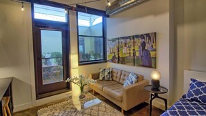 A modern living room with a sofa, a small table with a lamp, a painting on the wall, and large windows. - Chic Ultramodern Minimalist Studio Loft + Patio (Saint Louis)