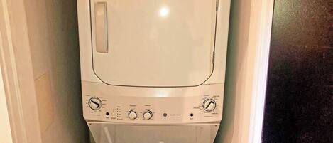 Lavadora blanca compacta en un espacio reducido, con un panel de control que incluye varios diales y botones.