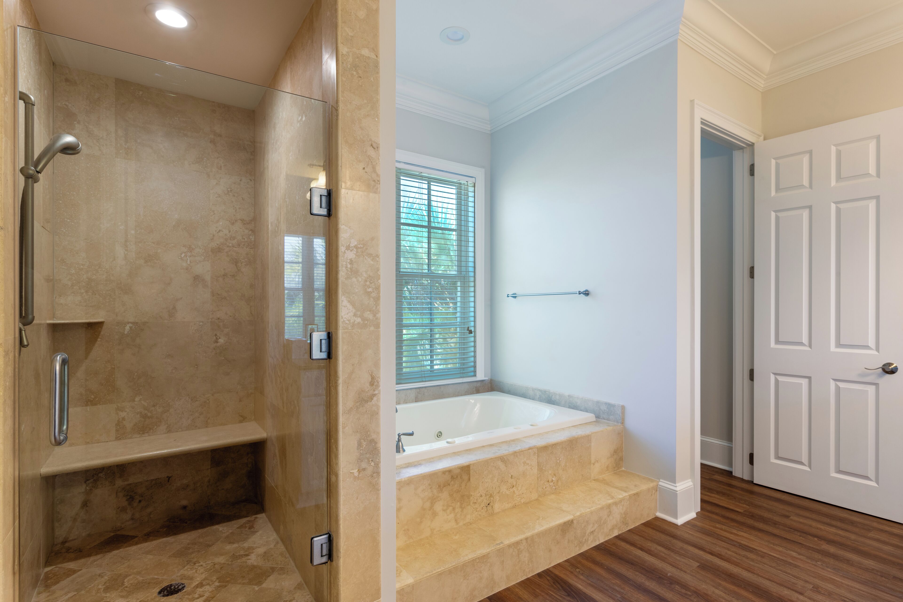 Une salle de bain avec une douche à l’italienne, une baignoire et une fenêtre avec des stores.
