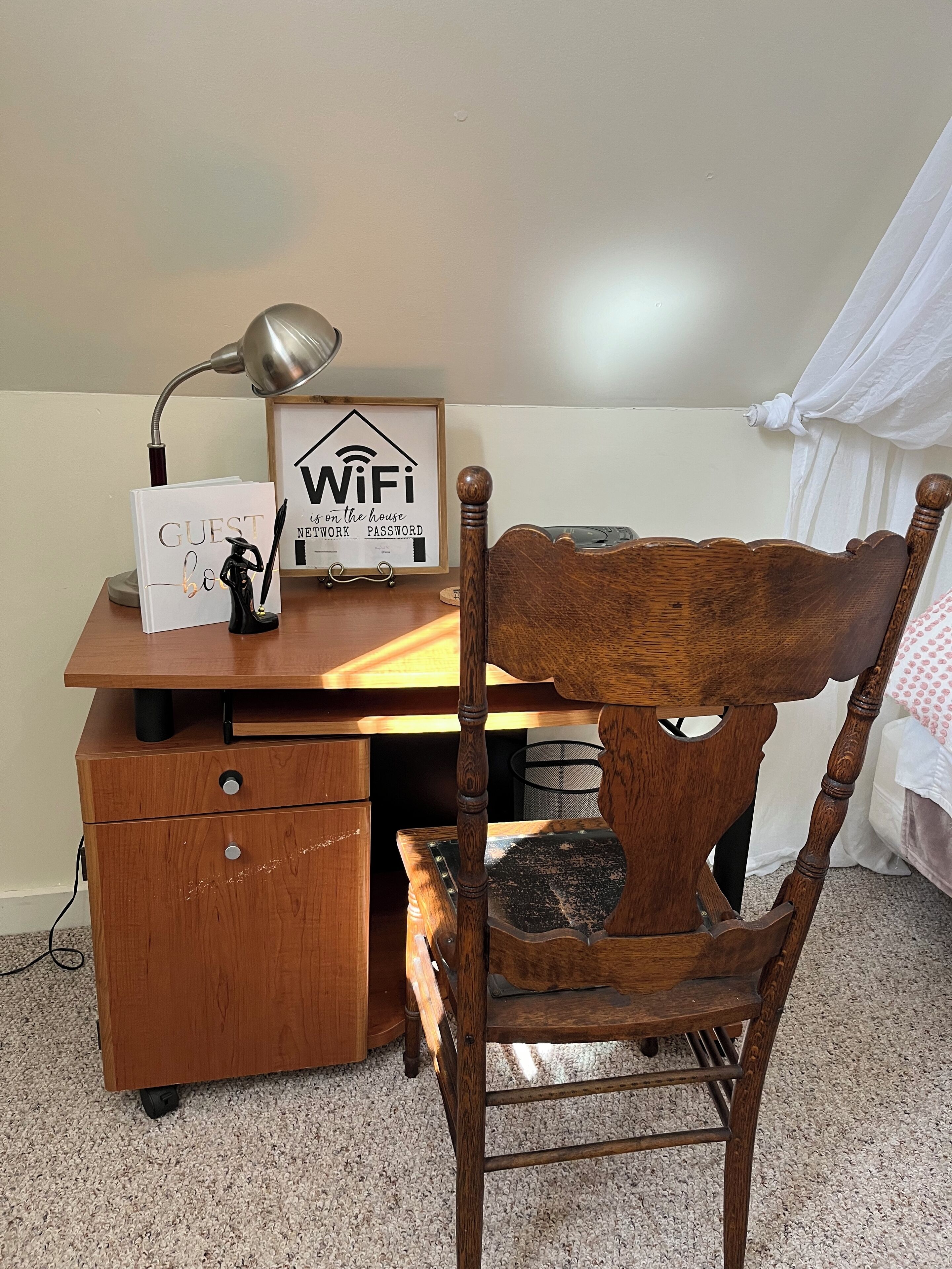 A wooden desk with a lamp, a framed sign reading "WiFi in the house," and a small figurine.