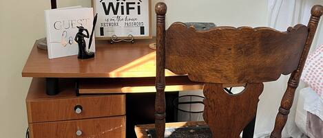 A wooden desk with a lamp, a framed sign reading "WiFi in the house," and a small figurine.