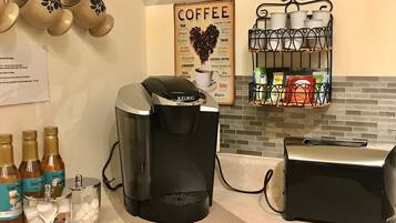 A kitchen with a coffee maker, a toaster, and a coffee menu on the wall.