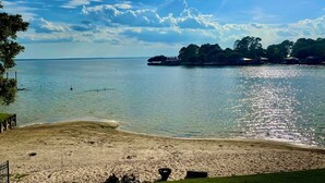 A beach with clear water, a sandy shore, and a distant island with buildings.