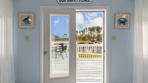A door with a sign reading "OUR HAPPY PLACE" leading to a balcony with a view of a dock and boats.