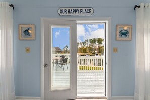 A door with a sign reading "OUR HAPPY PLACE" leading to a balcony with a view of a dock and boats.