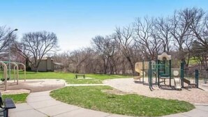 A park with playground equipment, a walking path, and a building in the background. - Private Suite with Nature Views (Omaha)